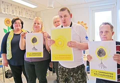 Sastamalan Toimintakeskuksen asiakkaat Sini Aalto, Viktor Rabkov ja Timo Neronen esittelevät eri versioita Vammaisten Kulttuuriviikon tämän vuoden logosta, auringonkukasta. Viktorin hyppysissä on hänen oma luomuksensa. Kuvassa vasemmalla Marika Kilkkinen ja Viktorin olan takaa kurkistaa Maija Jokinen.